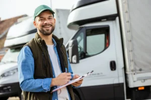 Man smiling and signing a document, standing in front of two trucks.