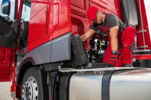 A truck mechanic in red overalls repairs a truck for a client who got a truck repair loan to keep his vehicle in working condition